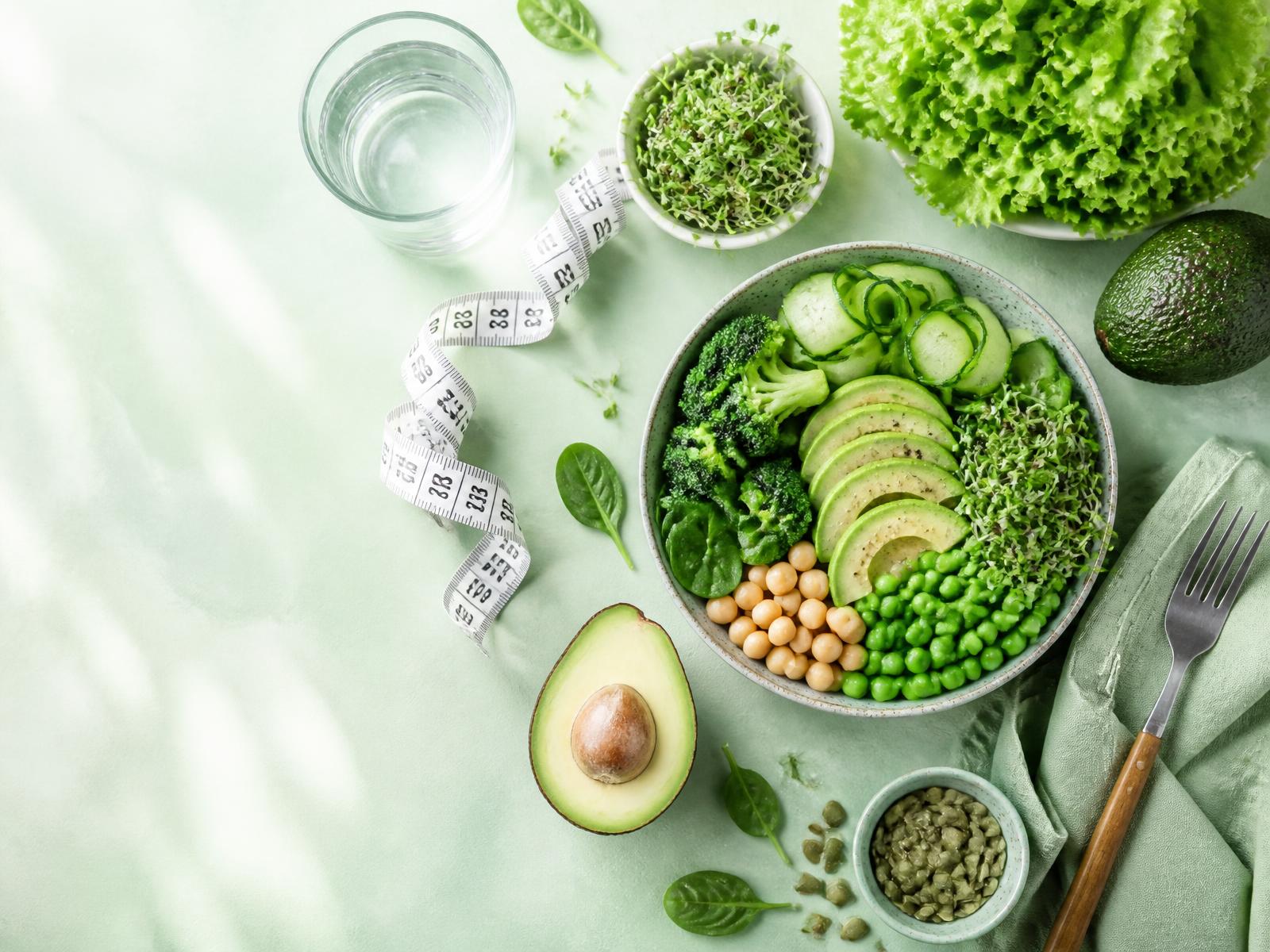 Fresh green vegetables, salad bowl and measuring tape on a pastel green surface